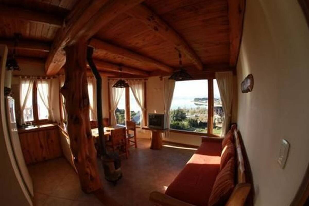 A cozy wooden interior with a sofa, TV, and dining area, overlooking a scenic view.