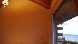Un dormitorio con techo de madera, una cama con almohadas, una mesita de noche y vistas al exterior.