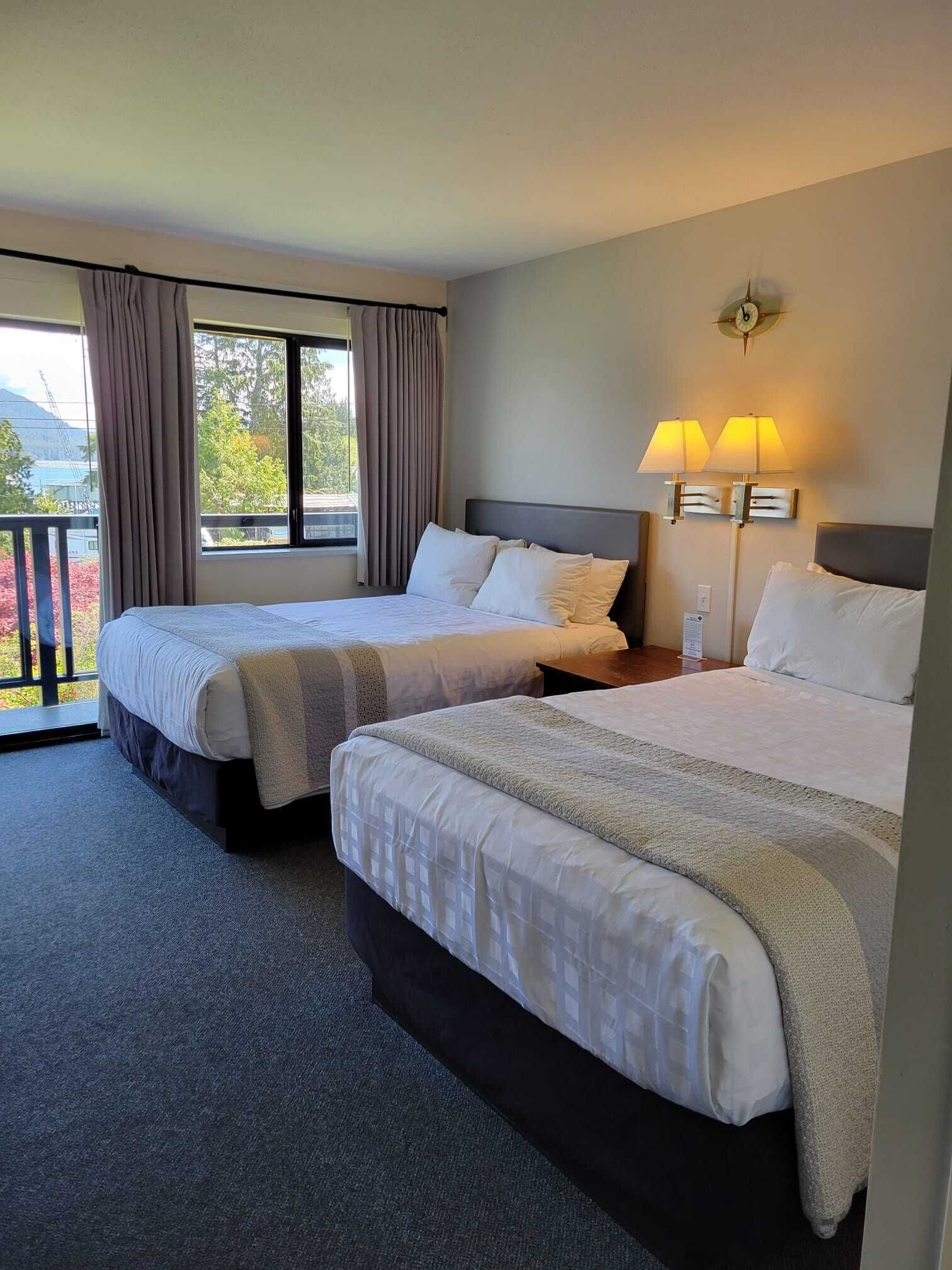 A hotel room with two beds, a balcony, and a view of the outdoors.