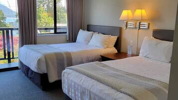 A hotel room with two beds, a balcony, and a view of the outdoors.