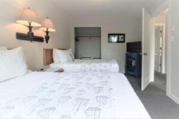 A hotel room with two beds, a wardrobe, a television, and a wall-mounted lamp. - Tofino Motel Harborview (Tofino)