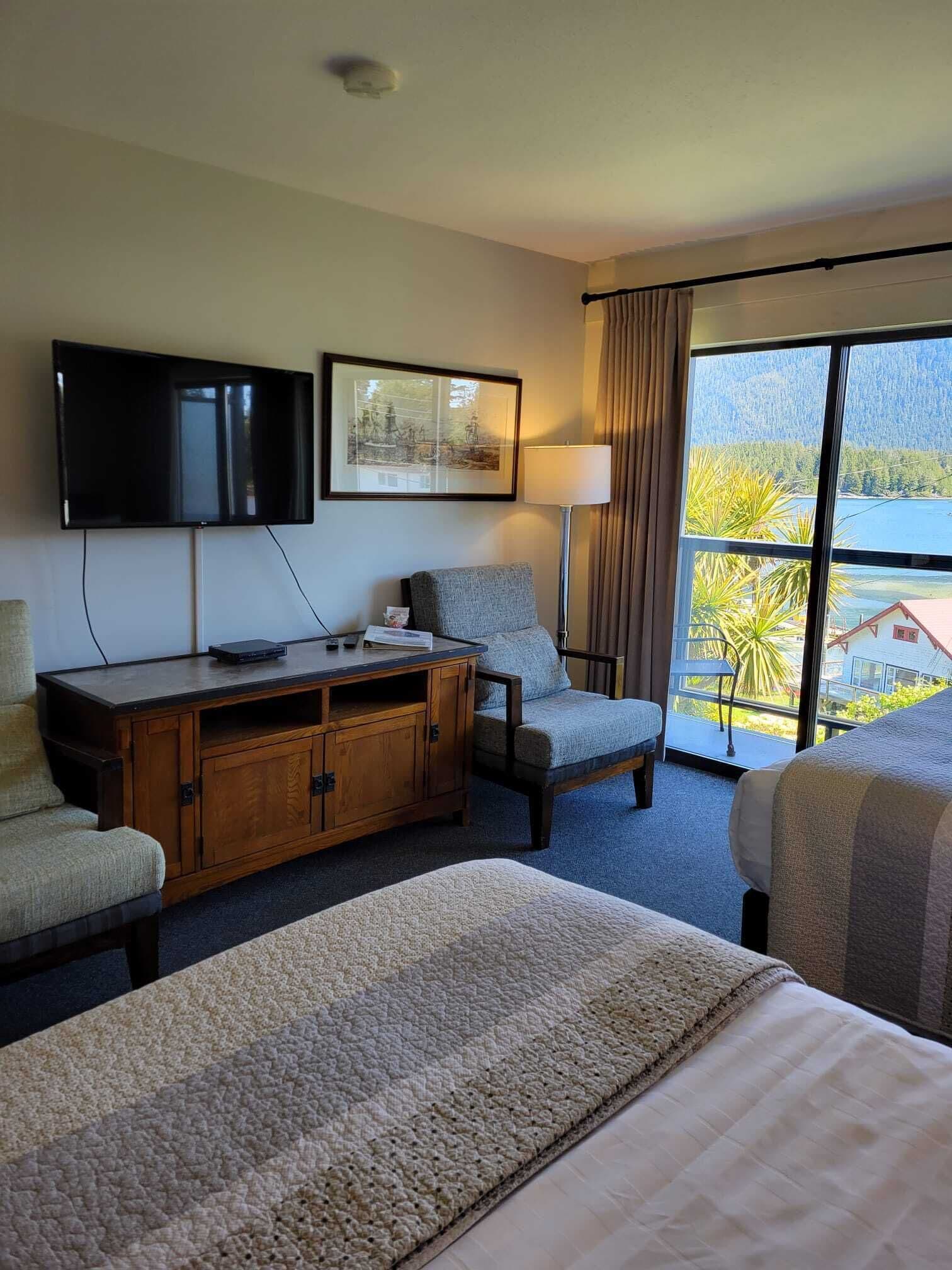 A hotel room with a bed, a desk, a chair, a television, a painting, a lamp, and a view of the outdoors.