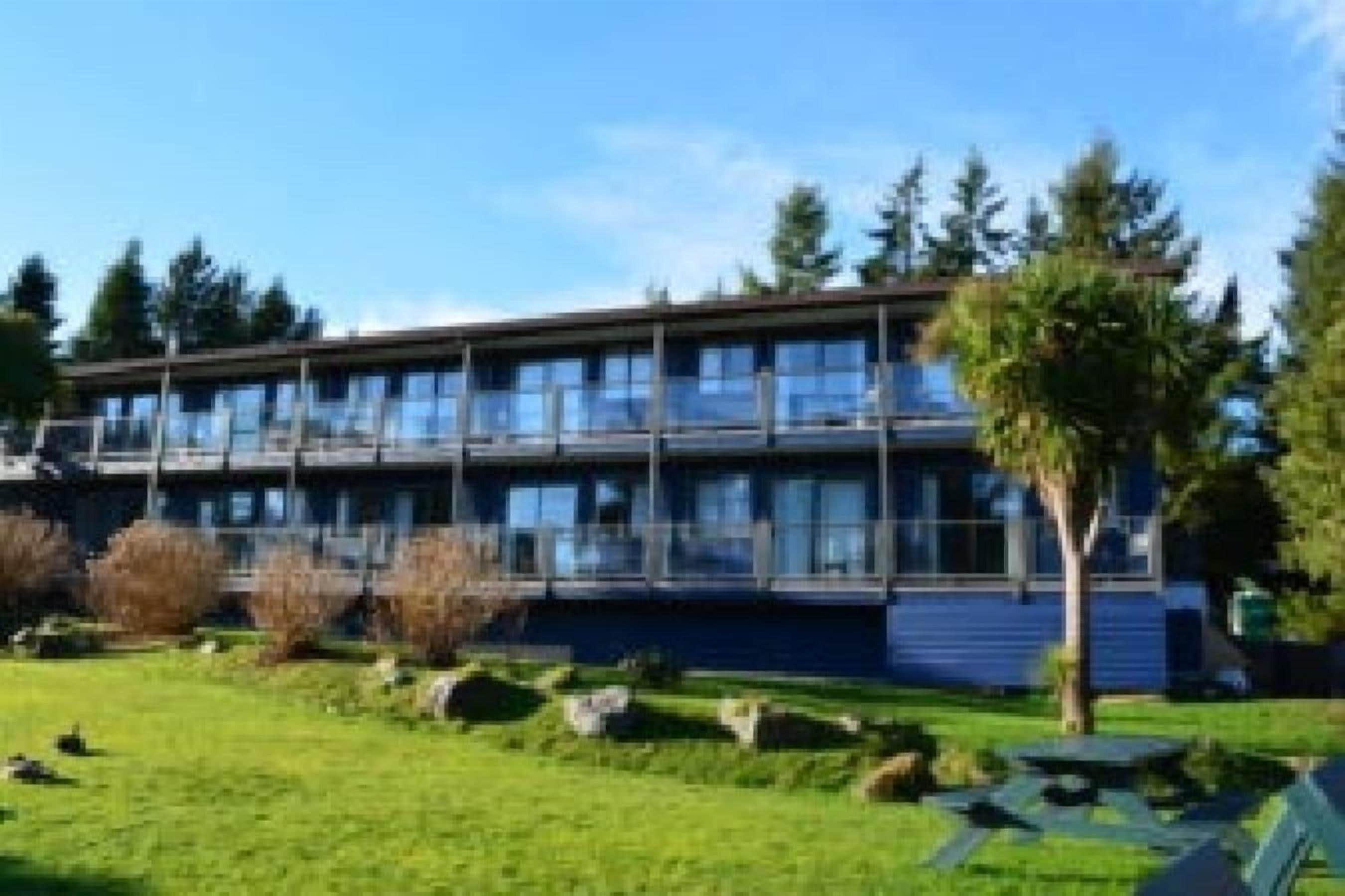 A modern building with multiple floors, large windows, and a well-maintained lawn with trees and shrubs.