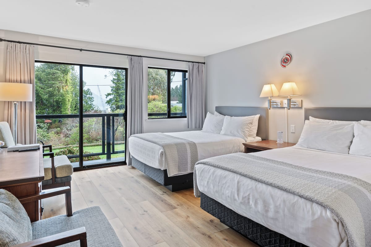 Ein Hotelzimmer mit zwei Betten, einem Schreibtisch und Blick auf Grün durch große Fenster.