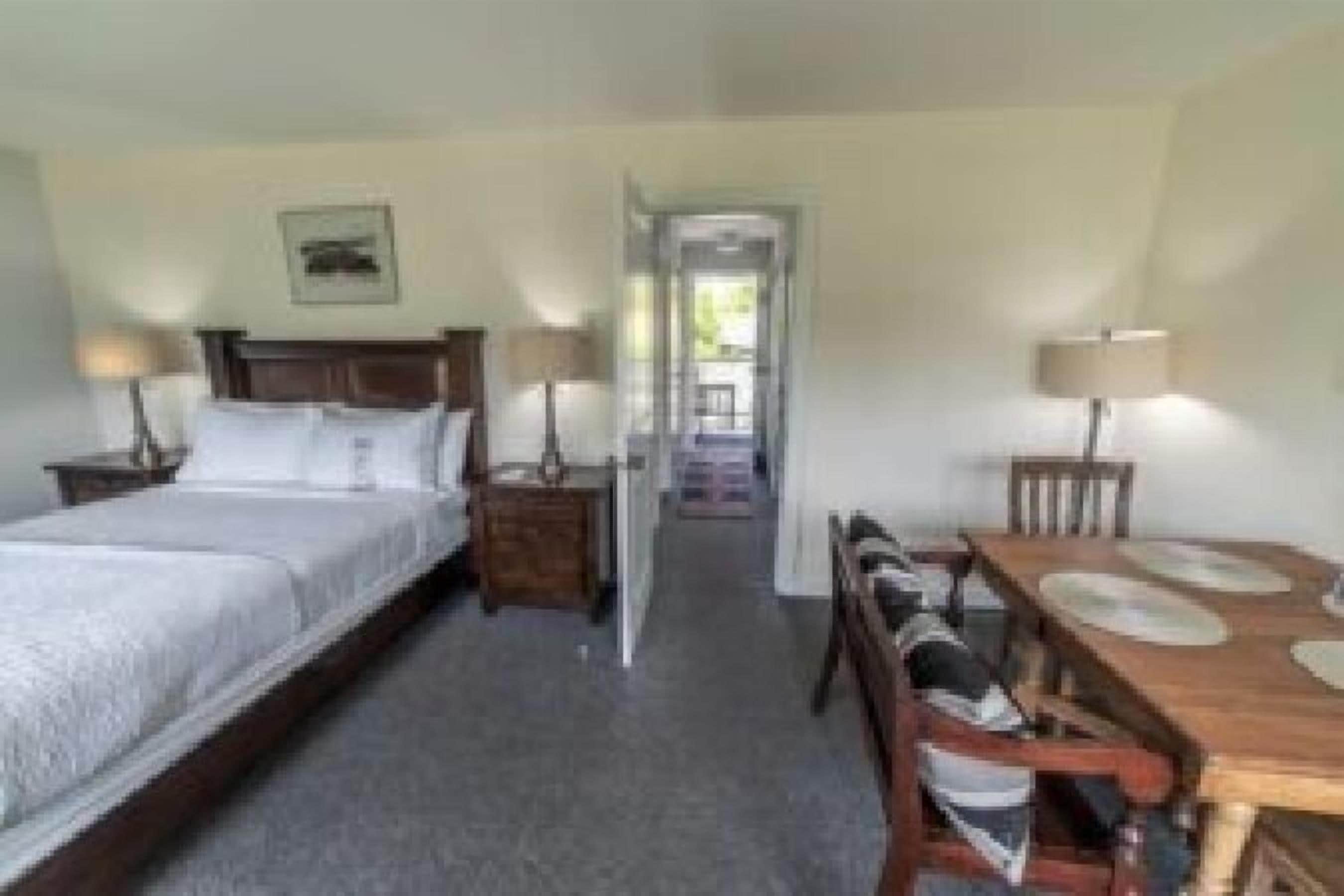 A hotel room with a bed, bedside tables, a desk with chairs, and a dining table.