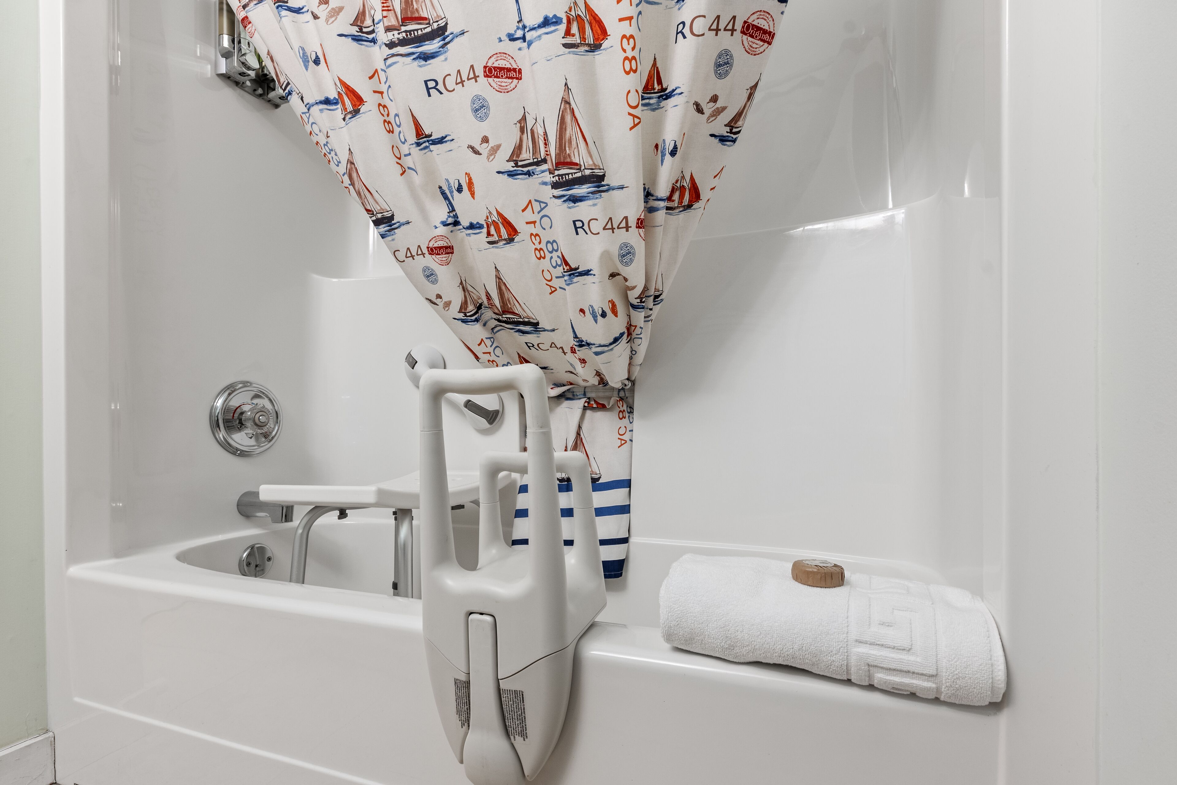 Une baignoire blanche, équipée d’un siège de douche, d’une serviette et d’un rideau orné de motifs de voiliers.