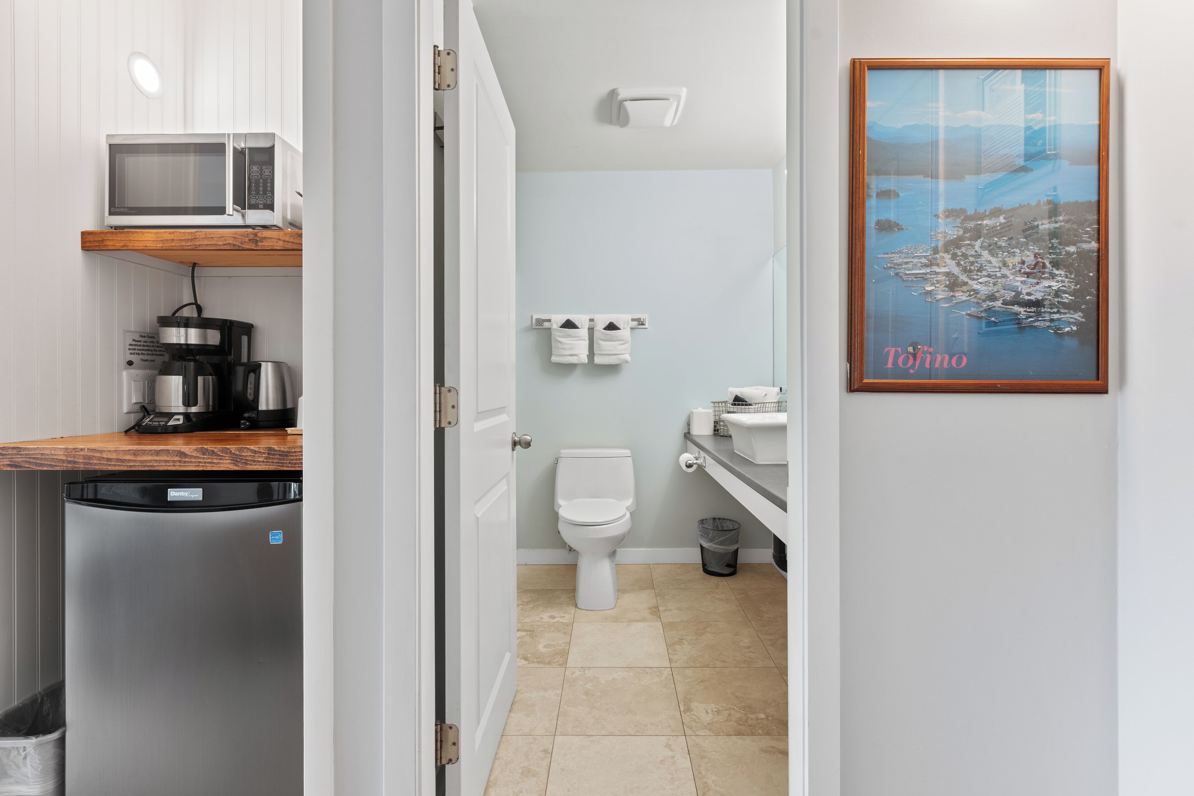 A compact kitchen with a microwave, coffee maker, and refrigerator. A bathroom with a toilet and sink is visible through an open door.