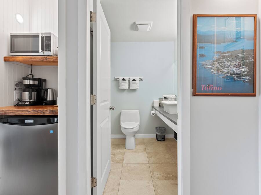 A compact kitchen with a microwave, coffee maker, and refrigerator. A bathroom with a toilet and sink is visible through an open door.
