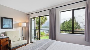 A hotel room with a bed, a chair, a desk with a lamp, and large windows offering a view of greenery and a body of water. - Tofino Motel Harborview (Tofino)