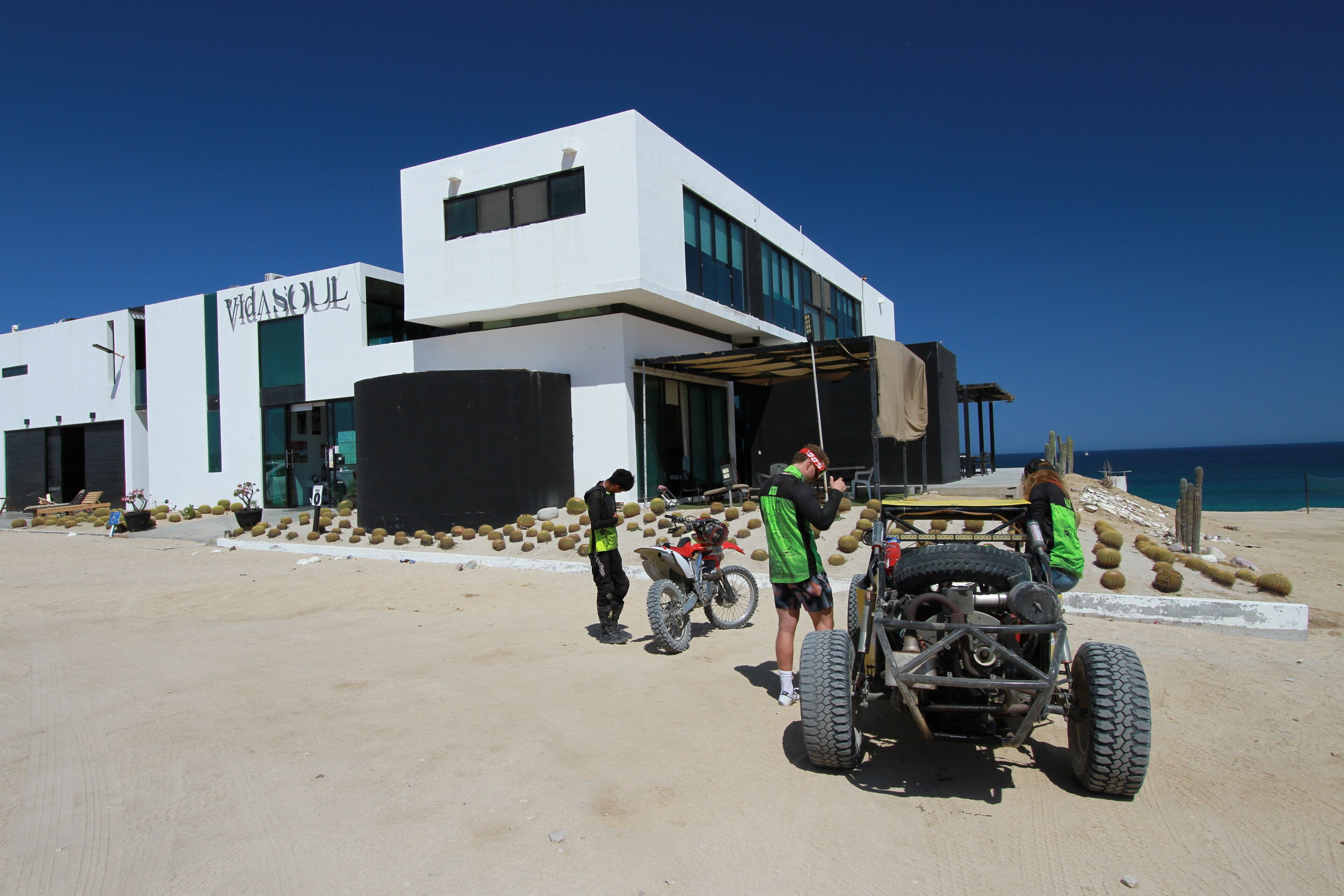A modern building with a sign 'Villasoul' and a dirt ground with vehicles.