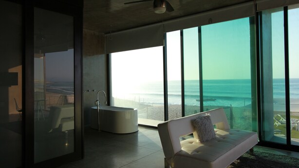 Un interior moderno con un ventanal grande con vista al océano, una bañera y un sofá con un cojín.