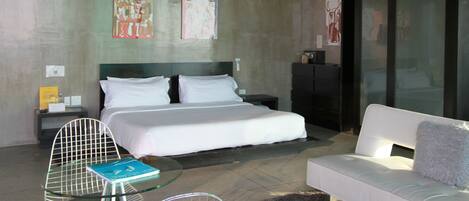 A hotel room with a bed, a glass table, a white sofa, and artwork on the walls.