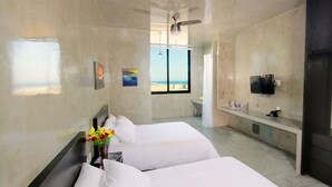 Habitación de hotel con dos camas, televisión, escritorio y vista a la playa.