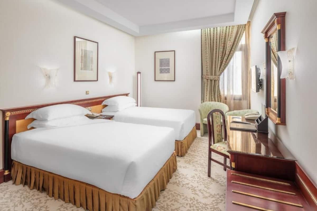 Une chambre d’hôtel avec deux lits, un bureau, une chaise et un miroir.