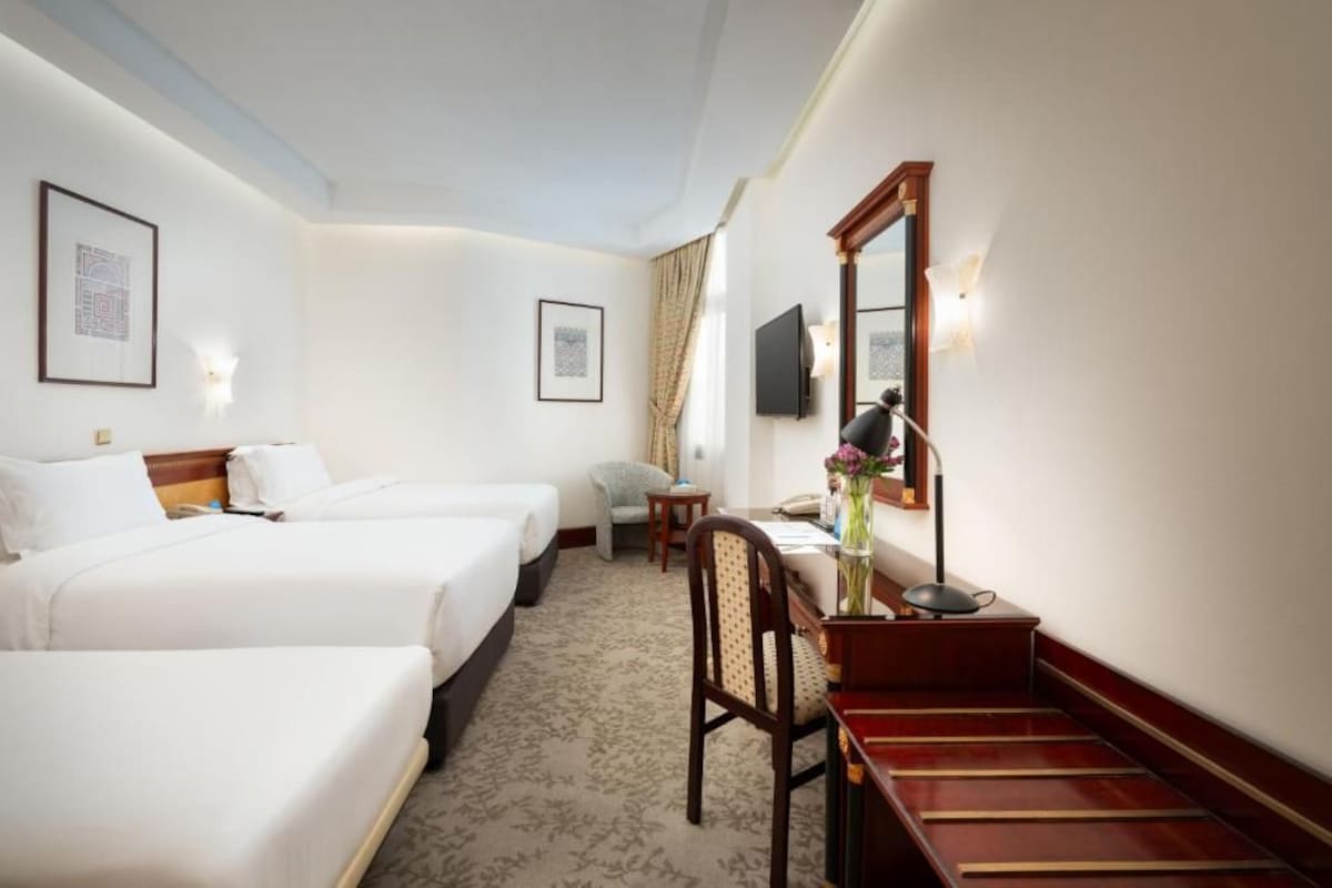 Una habitación de hotel con dos camas, un escritorio con silla, un televisor de pantalla plana y cuadros en las paredes.
