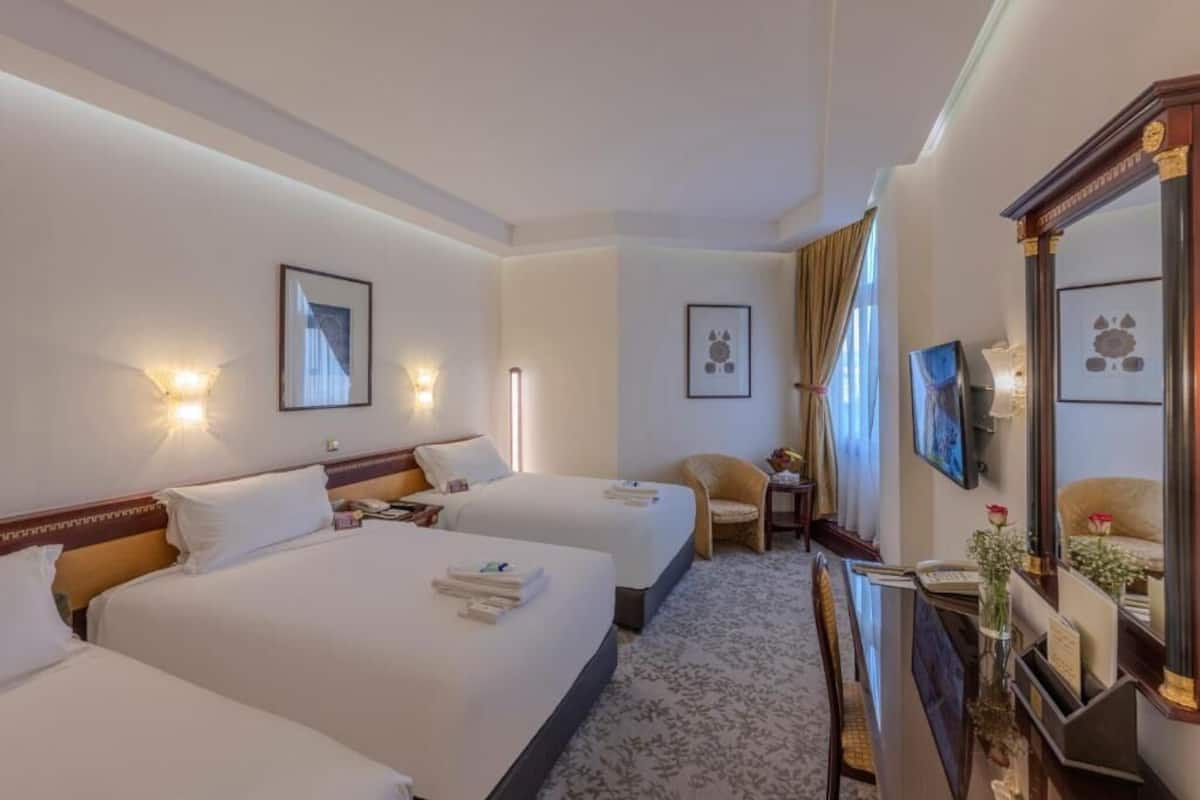 Une chambre d’hôtel avec deux lits, un bureau, une chaise et un téléviseur.