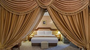 Een luxueuze slaapkamer met een groot bed, sierlijke gordijnen en een ingelijst schilderij aan de muur.