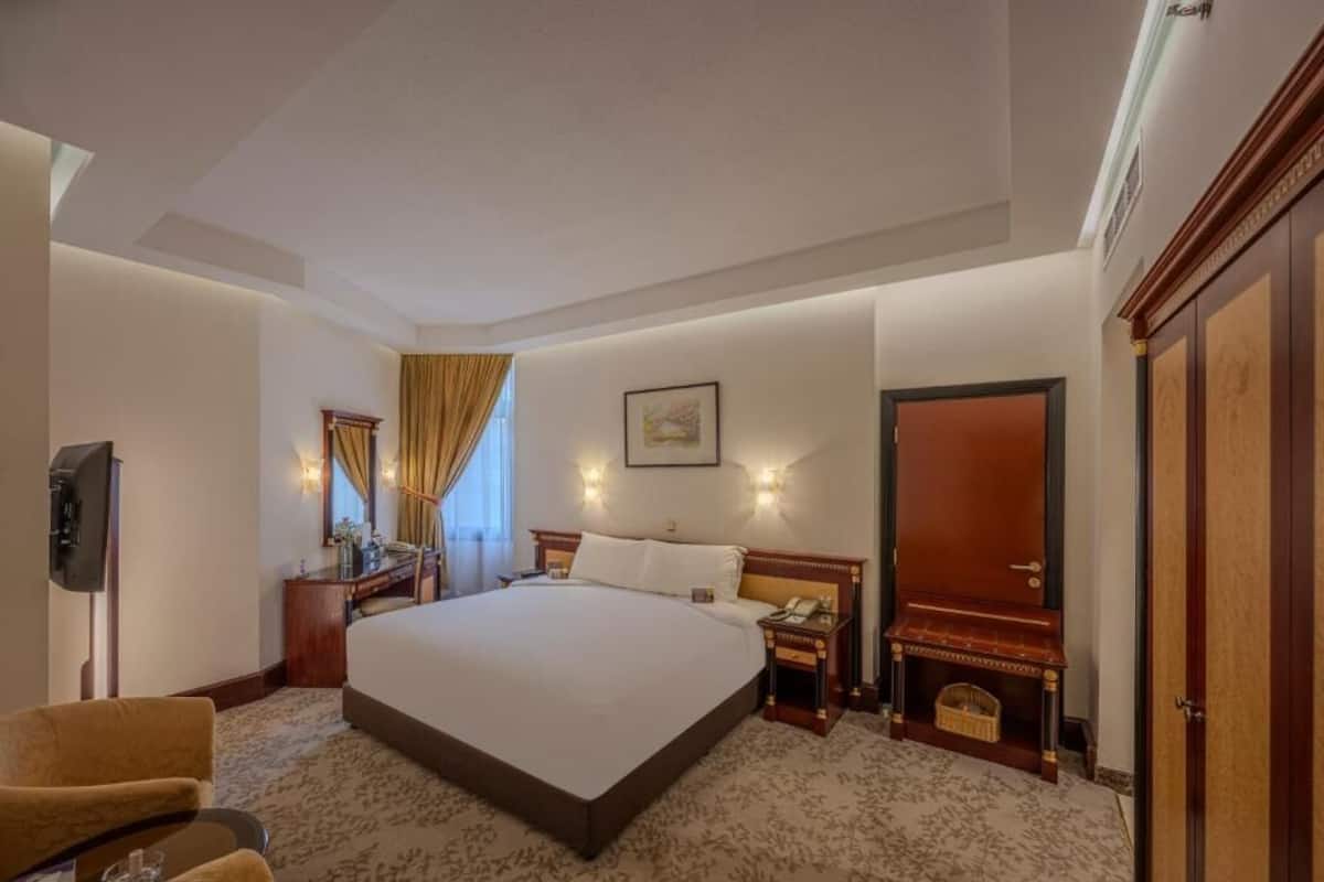 Une chambre d’hôtel avec un grand lit, un bureau avec un téléphone, une télévision et une petite table avec un panier.