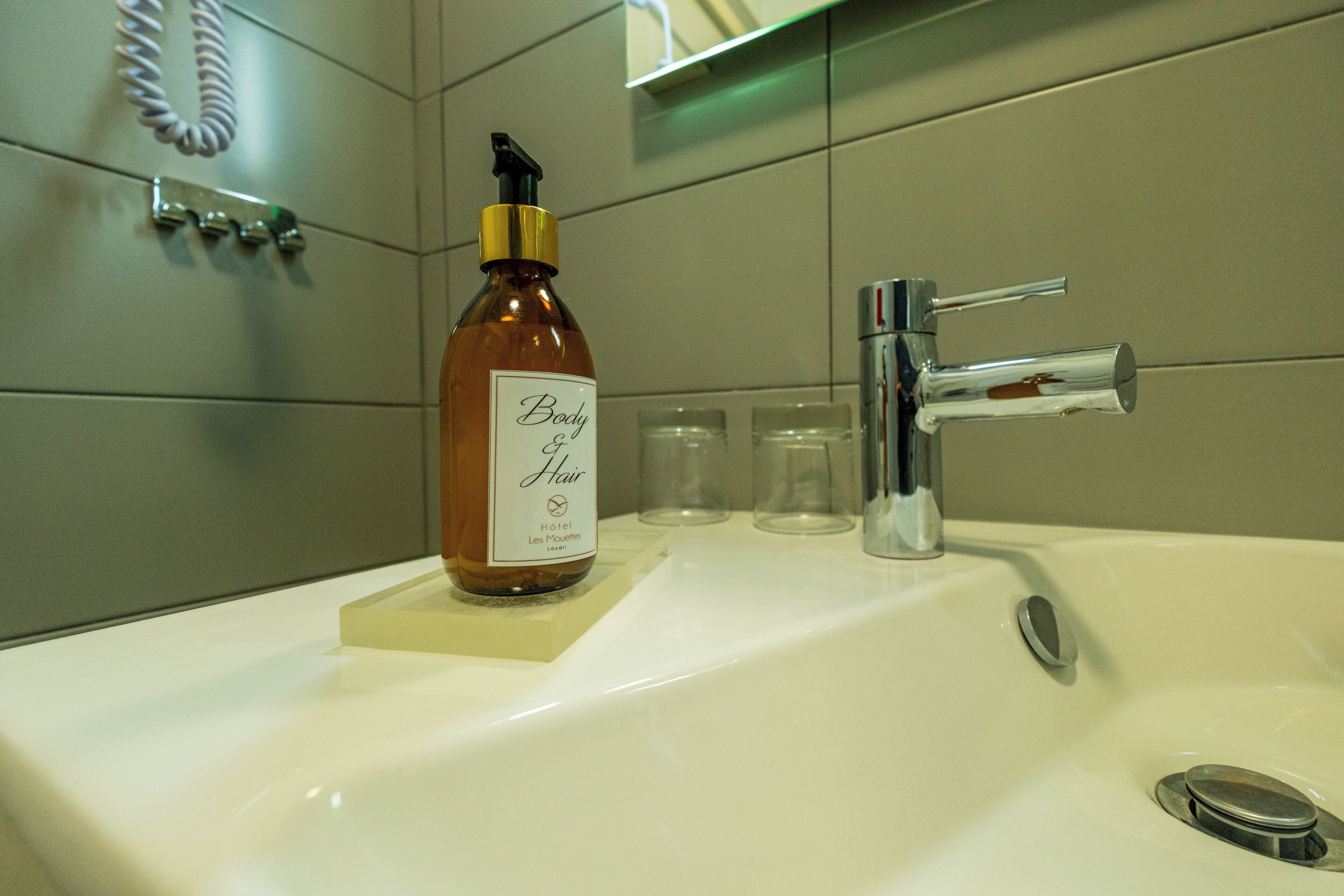 A bathroom sink with a bottle of body hair product, a faucet, and a hand dryer.