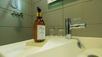 A bathroom sink with a bottle of body hair product, a faucet, and a hand dryer.