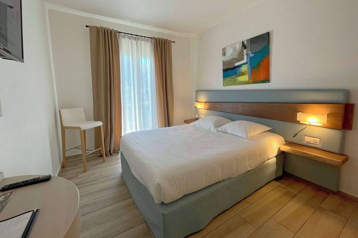 Ein Hotelzimmer mit einem Bett, Nachttischen, einem Sessel und einem Bild an der Wand.