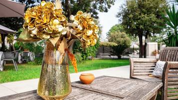 A rustic outdoor setting with a wooden table, a vase with golden decorative elements, and a clay pot.