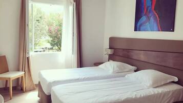 A hotel room with two beds, a window with curtains, a chair, and a painting on the wall.