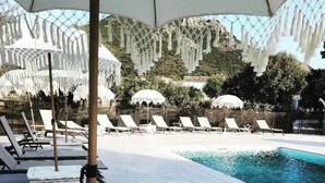 Un área junto a la piscina con sillones reclinables y sombrillas.