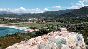 Un paisaje costero con primer plano rocoso, una playa y un pueblo a lo lejos.