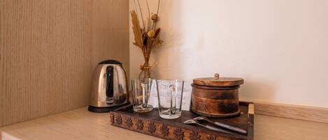 A wooden tray with a kettle, two glasses, a vase with dried flowers, and a wooden container on a wooden surface.