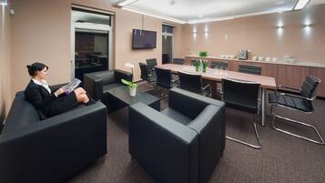 Una sala conferenze moderna con un lungo tavolo, sedie in pelle nera, un televisore a schermo piatto e un angolo caffè.