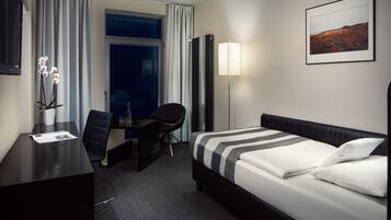 Una habitación de hotel con cama, escritorio, silla y un ventanal grande.