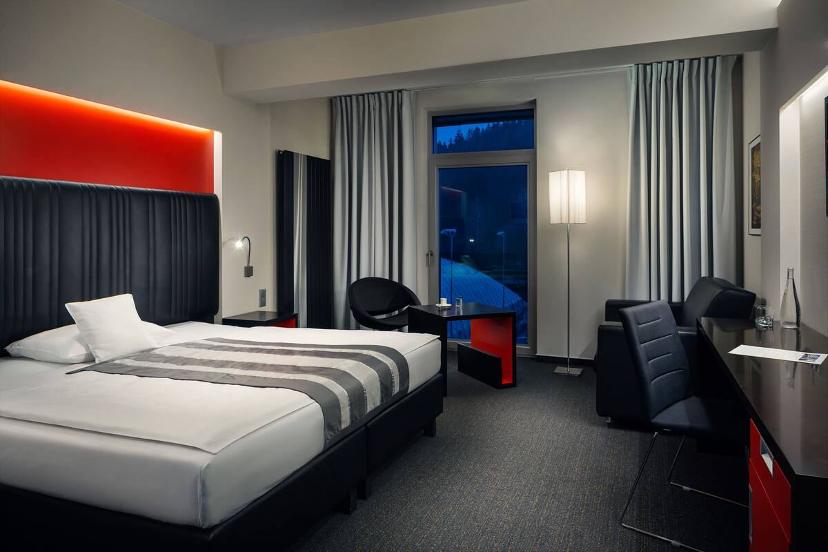 A hotel room with a large bed, a desk, a chair, and a view of the outdoors.