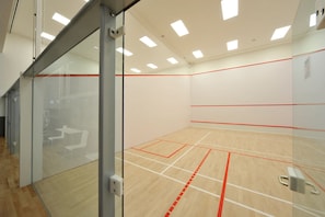 Una cancha de squash con paredes de vidrio, suelo de madera y líneas rojas que delimitan el campo.