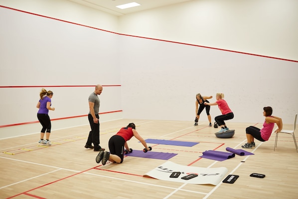 Un gimnasio con piso de madera, colchonetas de ejercicio y pared roja.