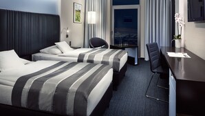 A hotel room with two beds, a desk, a chair, a TV, and a window with curtains. - Hotel Davídek (Trutnov)