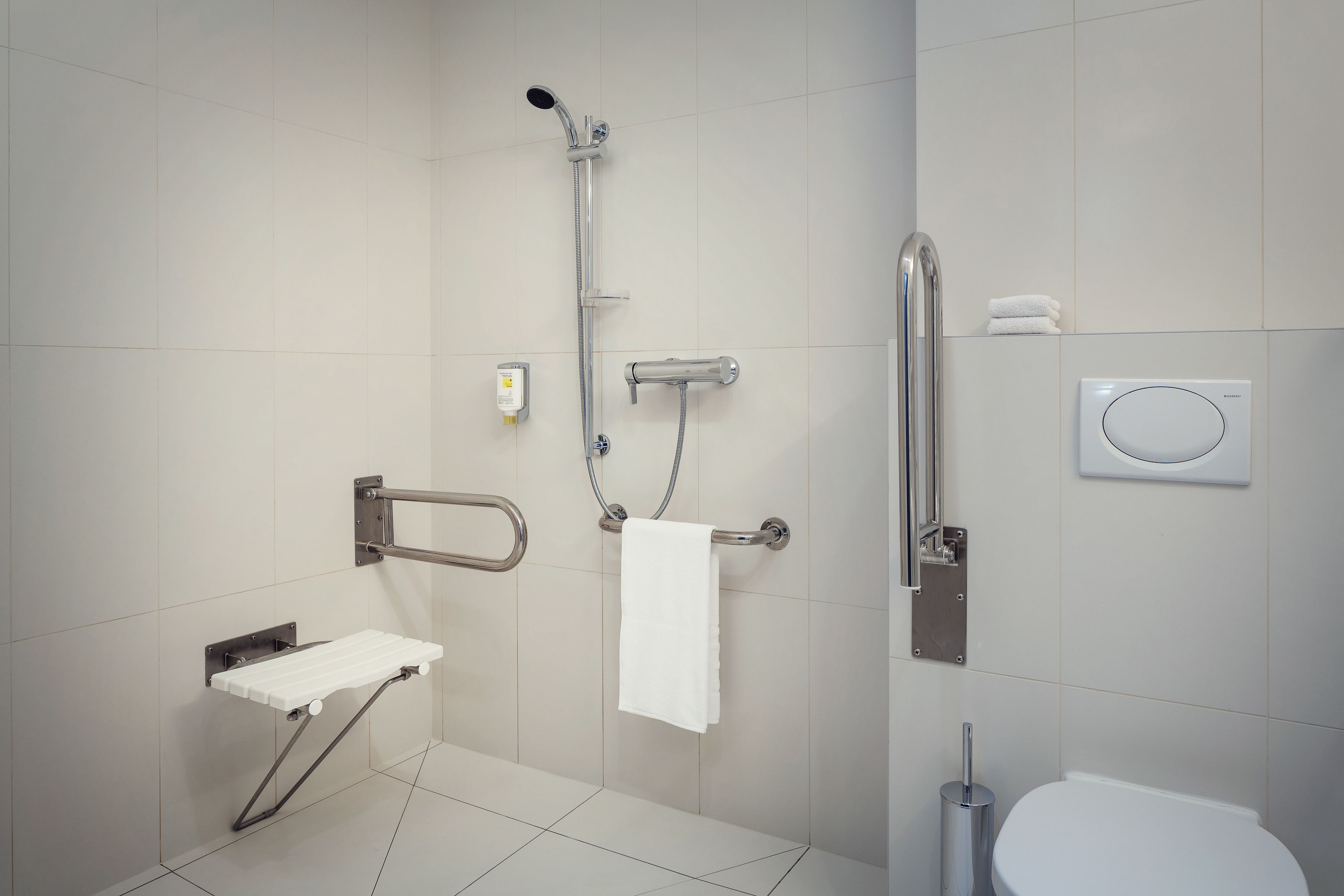 A modern bathroom with a shower, toilet, and grab bar.