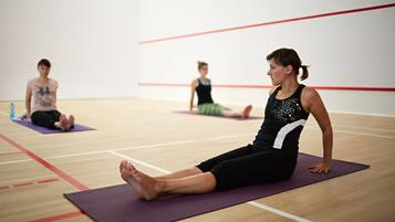 A gym with three people on exercise mats, wooden flooring, and a white wall with red lines.