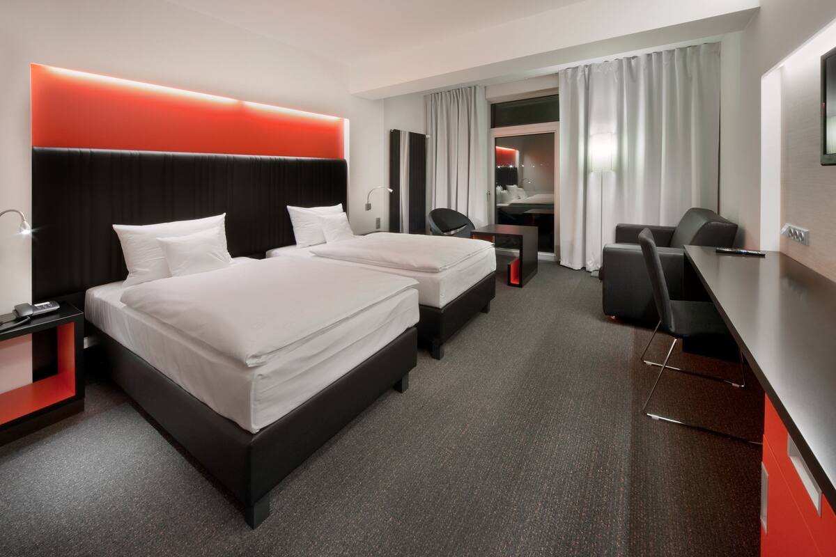 A hotel room with two beds, a desk, a chair, and a TV.