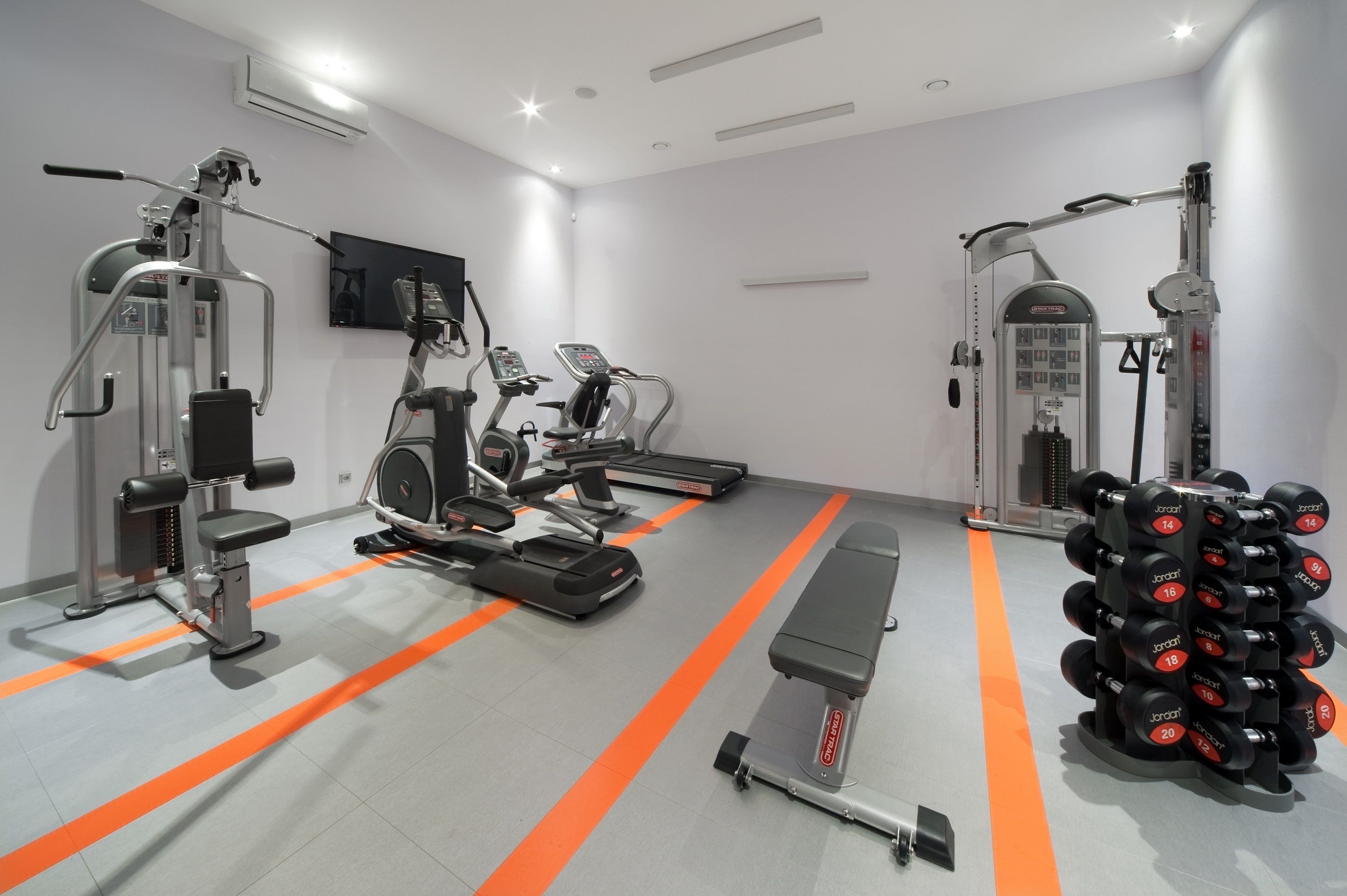 Un gimnasio moderno con máquinas de cardio, equipo de levantamiento de pesas y una banca.