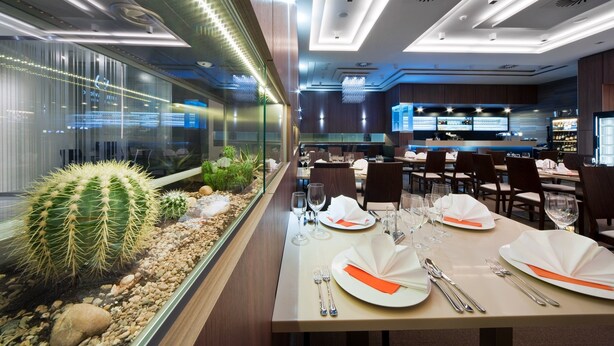 A restaurant with a modern interior, featuring a cactus display, neatly set dining tables, and a bar area. - Hotel Davídek (Trutnov)