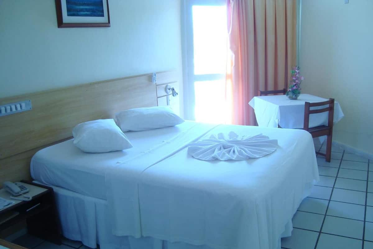 Una camera d'albergo con un letto, un comodino con un telefono, un tavolino con un vaso e una finestra con tende.