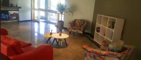 Un hall con sofás rojos, una pequeña mesa redonda y un sillón colorido.