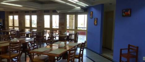 Un comedor con varias mesas y sillas de madera, ventanas amplias y paredes azules.