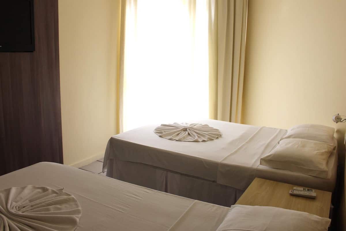 Una camera d'albergo con due letti, un comodino in legno e una finestra con tende.