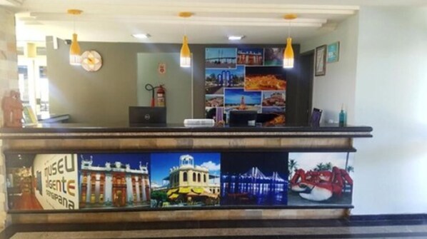 A reception desk with a computer, a fire extinguisher, and a wall decorated with various photographs. - Rede Andrade Aracaju (Aracaju)