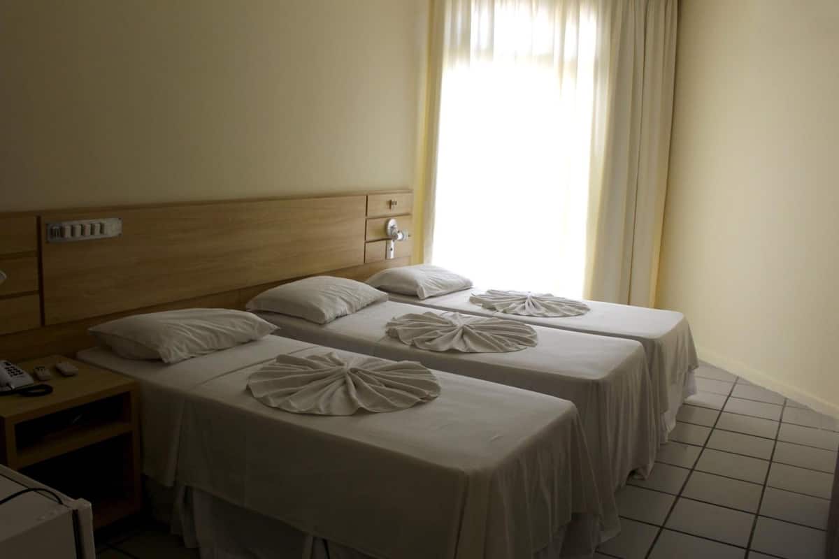 Camera d'albergo con due letti, ognuno dotato di cuscino e testiera decorativa. Si vede un comodino con un telefono e una lampada.