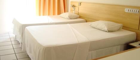 A hotel room with two single beds, a wooden headboard, a nightstand, and a window with curtains.