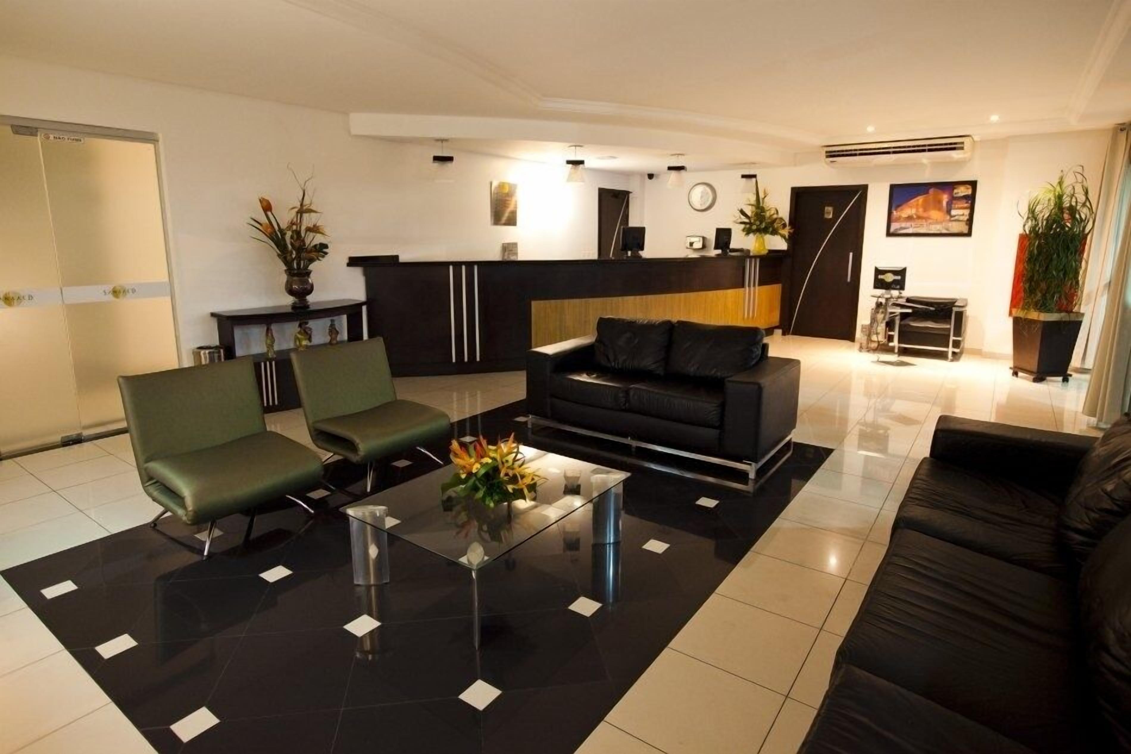Un moderno vestíbulo de hotel con mostrador de recepción, zona de estar con sofás y sillones, y una mesa de centro de vidrio.