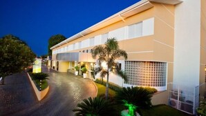 Een modern hotel met een gebogen oprijlaan, palmbomen en een goed verlichte entree.